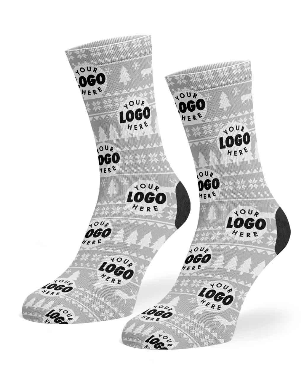 A pair of customizable crew socks with a light gray and white Nordic/Fair Isle pattern featuring snowflakes, Christmas trees, and reindeer. The socks have black accents on the heels and toes, with a black placeholder logo reading 'YOUR LOGO HERE' printed repeatedly across the surface.