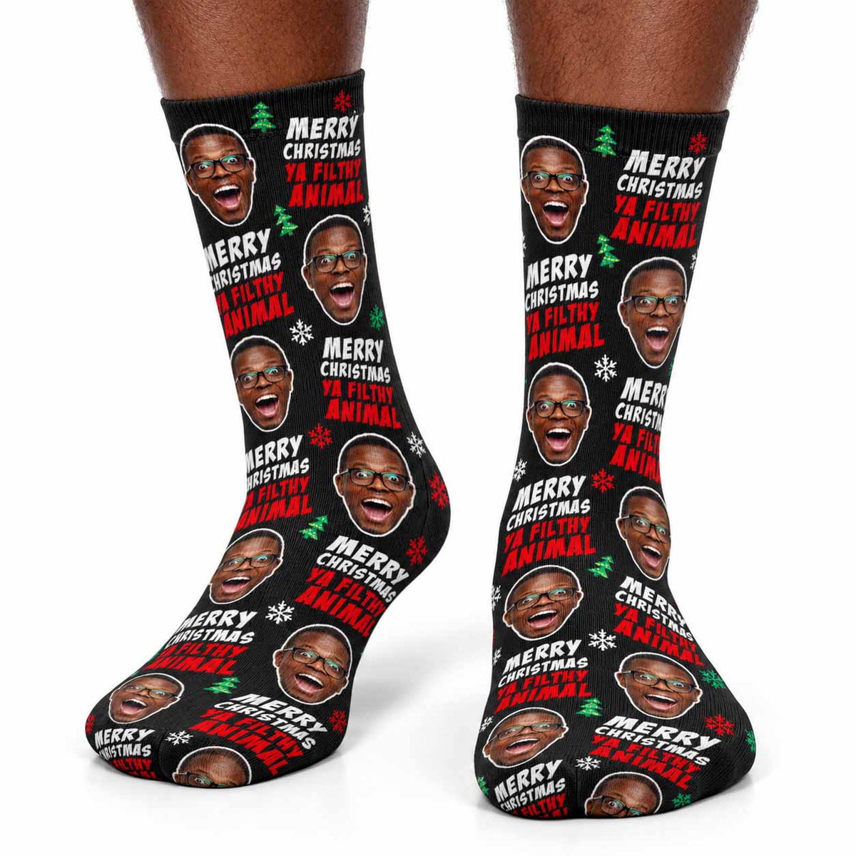 A pair of black crew socks with a repeating graphic print of a man's face and the text 'MERRY CHRISTMAS YA FILTHY ANIMAL' in white and red, shown on a model's feet against a white background.